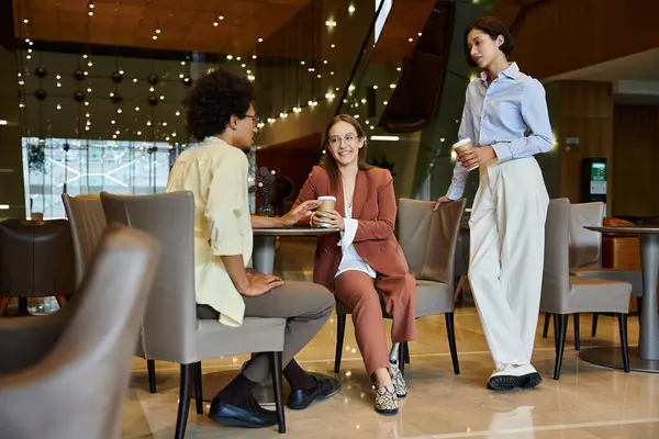 stock image Three diverse colleagues chat over coffee during a break in a modern office setting.