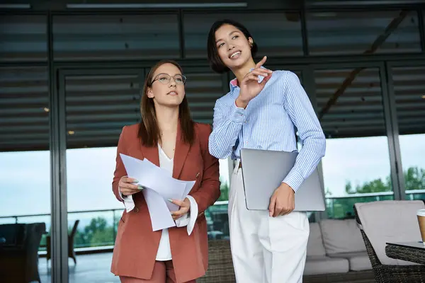 stock image Two colleagues chat and work on documents while enjoying the view from their modern office rooftop.