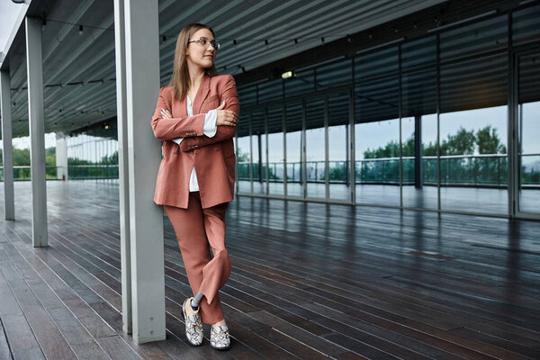 A woman with a prosthetic leg leans against a pillar on a modern office rooftop terrace