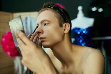 Bir travesti performansından önce sahne arkasında aynaya bakarken makyaj yapar..