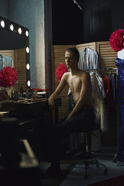 A drag performer sits in front of a vanity mirror, waiting for their performance.