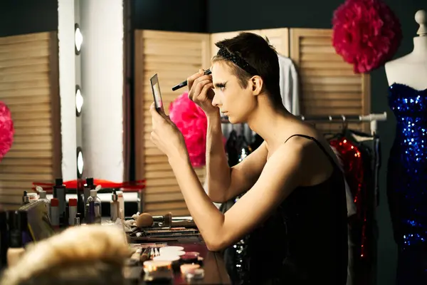 stock image A drag performer applies makeup while looking in a mirror, preparing for a performance.