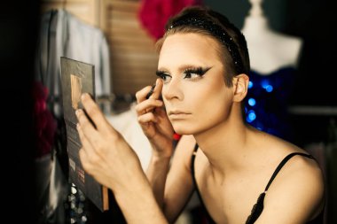 Bir travesti gösteriden önce sahne arkasına göz kalemi sürer..