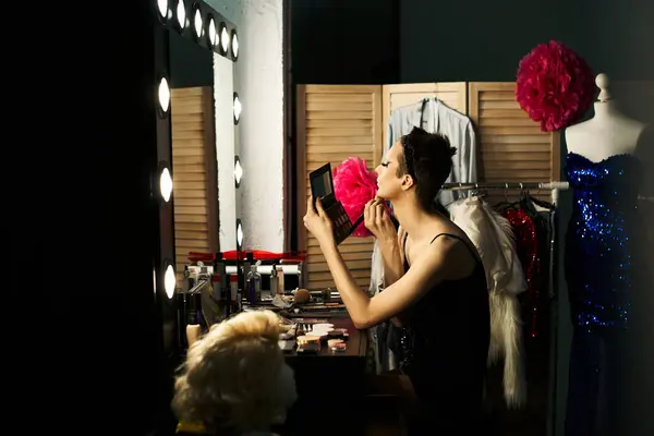 stock image A drag performer applies makeup at a dressing table in a backstage setting.