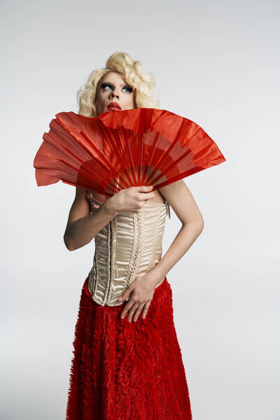 Королева трансвеститов в блондинистом парике, красной юбке и корсете резко позирует, держа перед собой красный веер..