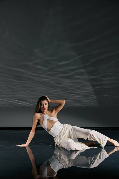 A young woman in a white outfit poses on a reflective floor, her long hair falling around her shoulders.
