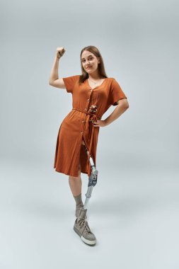 A woman with a prosthetic leg stands confidently in a studio, flexing her bicep. clipart