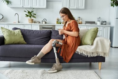 Protez bacaklı bir kadın koltuğa oturur, rahat bir şekilde telefonunu kullanır..