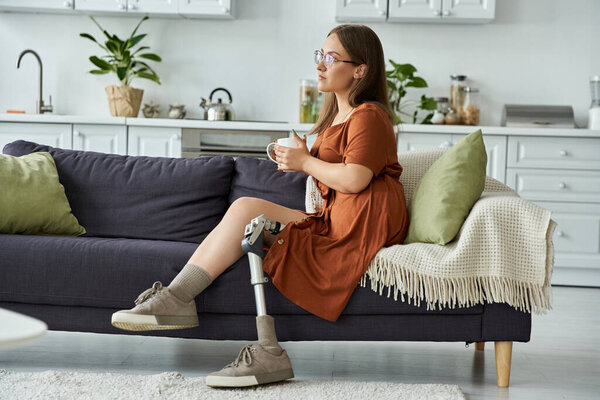 A woman in a rust-colored dress sits on a couch with a cup in her hand.