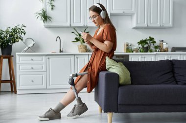 Kanepede oturan, kulaklık takan ve telefonuna bakan genç bir kadın..