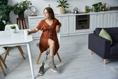 A woman in a brown dress sits at a kitchen table, her prosthetic leg visible. clipart