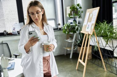 Kadın elinde kahveyle telefonunu kontrol ediyor.