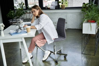 Protez bacaklı bir kadın masada oturur ve dizüstü bilgisayarla çalışır..