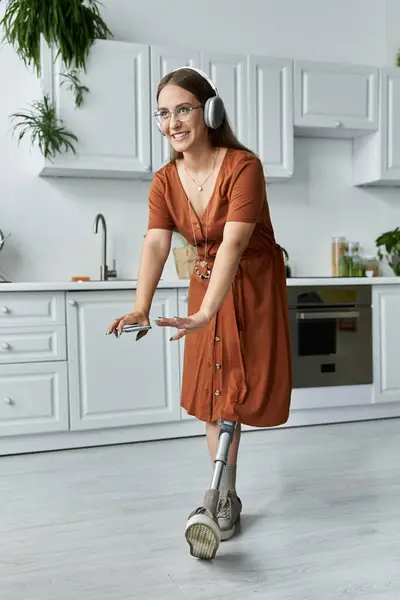 stock image A woman in a brown dress dances in a kitchen, wearing headphones and smiling.