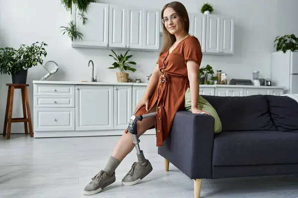 stock image A woman with a prosthetic leg sits on a couch in a modern kitchen.