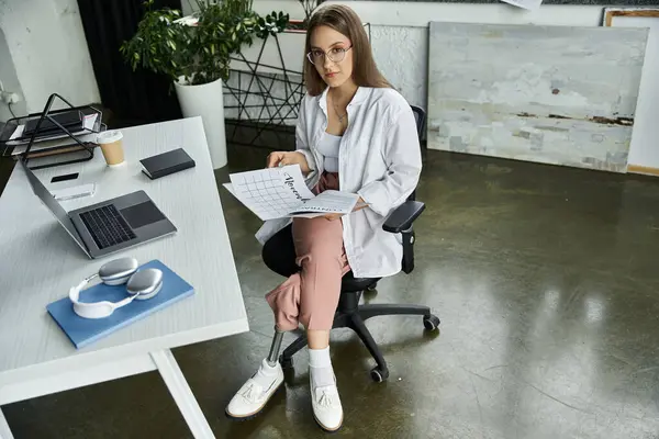 stock image A woman with a prosthetic leg sits at a desk, looking at the camera with a confident smile.