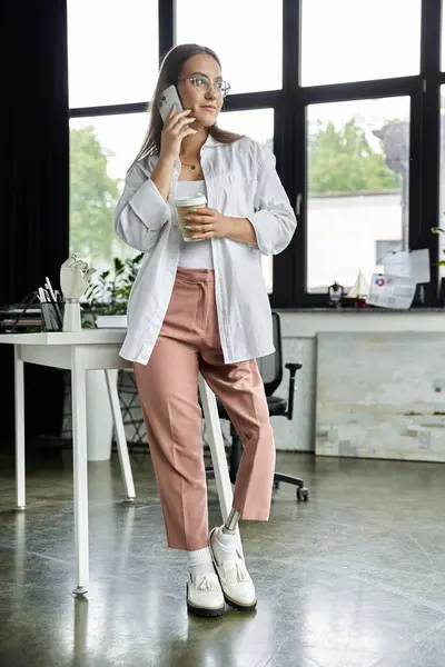 stock image A woman with a prosthetic leg talks on her phone while holding a cup of coffee.