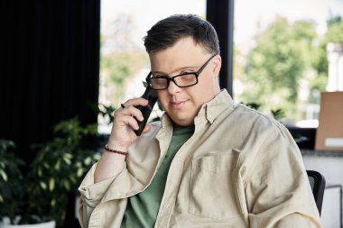 Down sendromlu genç bir adam sandalyede oturup telefonla konuşuyor..