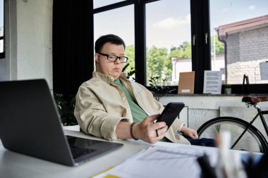 Down sendromlu genç bir adam masada oturmuş telefonunu kontrol ediyor..