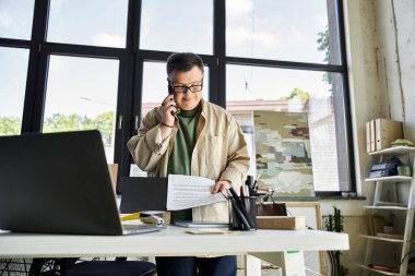 Down sendromlu gözlüklü genç bir adam masada beklerken telefonla konuşuyor..