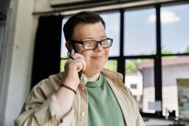 A young man with Down syndrome smiles while talking on a cell phone. clipart