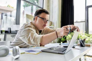 A young man with Down syndrome works on his laptop, focused on his task. clipart