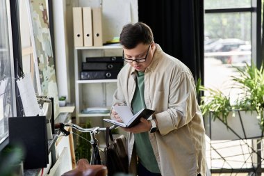 Young man with Down syndrome reviewing notes while standing near a bicycle. clipart