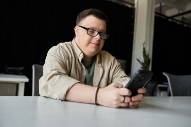 Down sendromlu genç bir adam telefonunu kullanırken gülümsüyor..