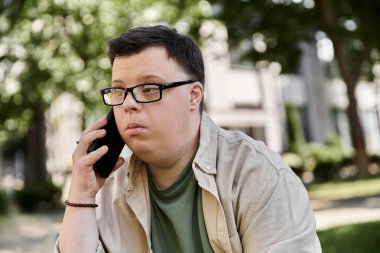 Down sendromlu bir adam dışarıda oturur ve telefonda konuşur..