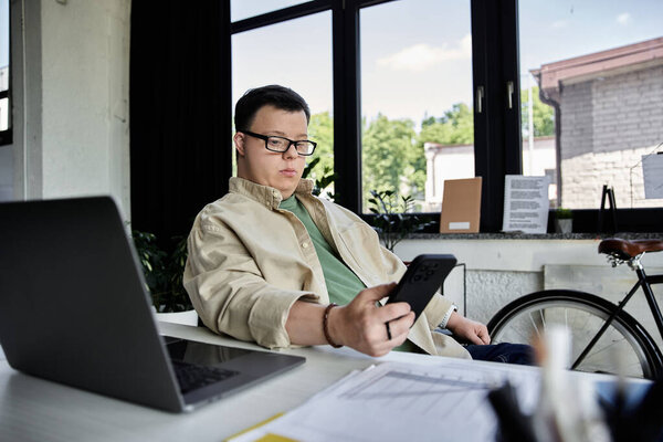 Молодой человек с синдромом Дауна сидит за столом и проверяет свой телефон.