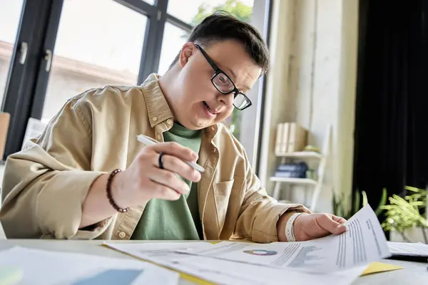 stock image A young man with Down syndrome reviews documents while sitting at a desk.