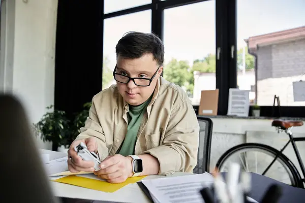 stock image A young man with Down syndrome sits at a desk, working on a task.