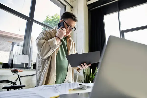 stock image A young man with Down syndrome, on the phone, looks at a folder while standing in an office.