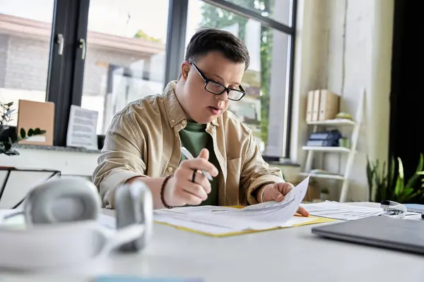 stock image A young man with Down syndrome sits at a desk, intently reviewing paperwork.