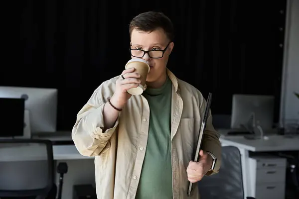 stock image Young man with Down syndrome sips coffee while holding a laptop.