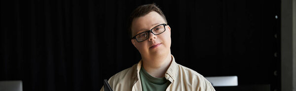 Молодой человек с синдромом Дауна улыбается в камеру.