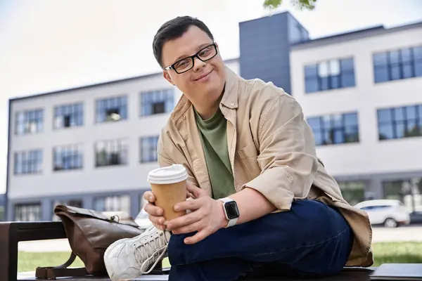 Stock image A man with Down syndrome sits on a bench, enjoying a cup of coffee.