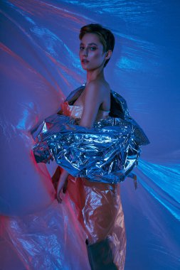 A woman poses against a blue background, wrapped in a silver, shimmering fabric. clipart