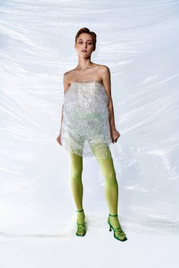 A woman stands in front of a white background, wearing a dress made from recycled plastic packaging.