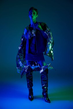 Bir kadın mavi ve gümüş bir elbiseyle neon ışıkların altında poz veriyor..