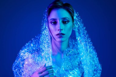 Mavi ve mor neon ışıkla yıkanmış sürdürülebilir bir moda ürünü içinde bir kadın..