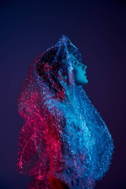 Kadın neon ışıklı odada, kafası arkaya eğilmiş, baloncuklu ambalaja sarılmış.