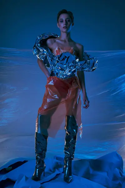 stock image A woman wearing a shimmering, recycled fashion piece stands against a backdrop of plastic sheeting.