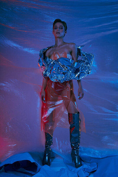 Женщина в футуристическом костюме стоит на сине-красном фоне из пластика.