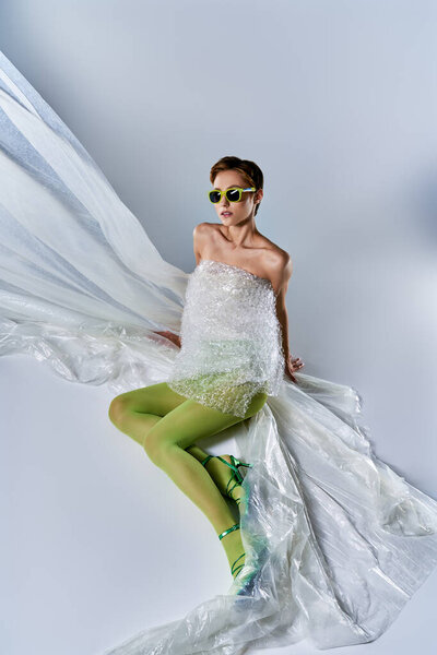 Woman in bubble wrap dress poses on white background, surrounded by plastic sheeting