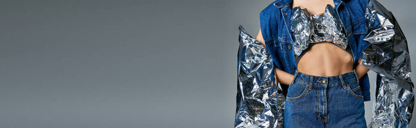 Женщина носит джинсовую куртку и джинсы с серебряной отражающей тканью на плечах.