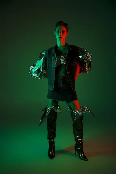 stock image Woman in denim jacket and knee-high boots stands in studio, lit by green and red neon lights