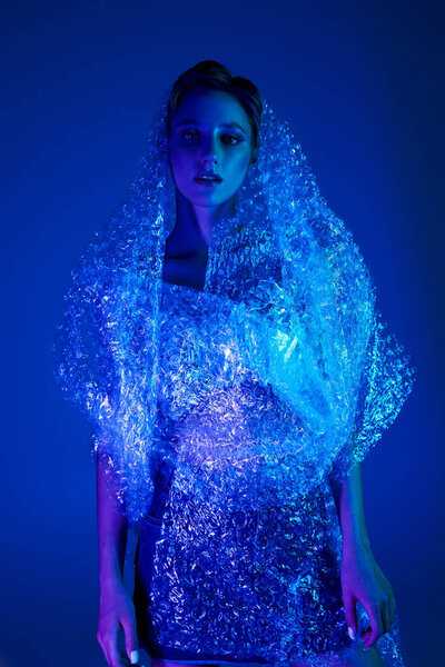 A woman wrapped in bubble wrap, illuminated by blue light, stares intensely at the camera.