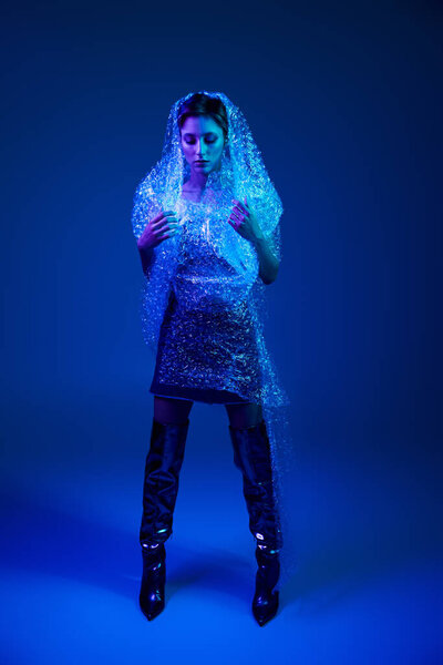 A woman stands against a blue backdrop, draped in bubble wrap as a sustainable fashion statement.