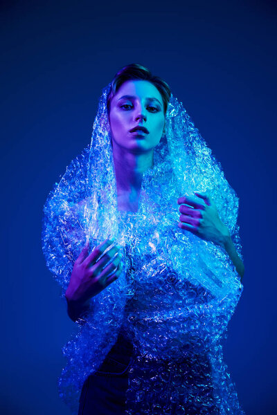 Woman in dress of bubble wrap stands in blue light